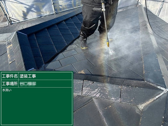 屋根の棟部分付近を高圧洗浄機で丁寧に洗浄している作業員の様子