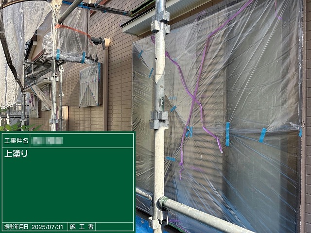 窓まわりに養生シートを施したうえで行っている外壁塗装工事の上塗り