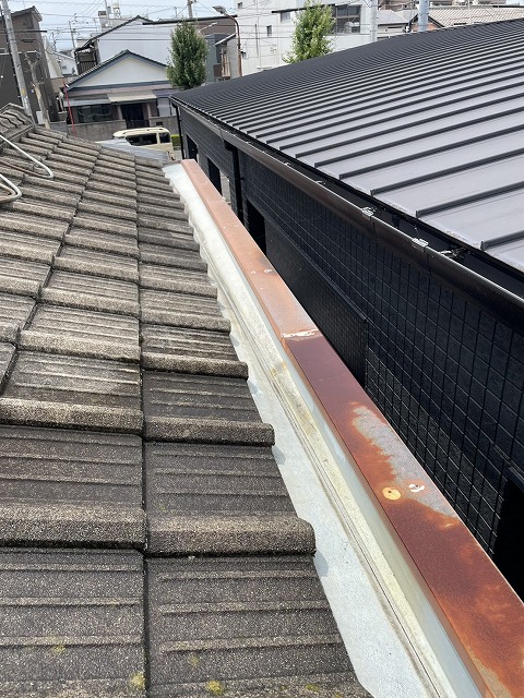 瓦屋根の端にパラペットと笠木があり、その間に谷板金が設置されている屋根の状態